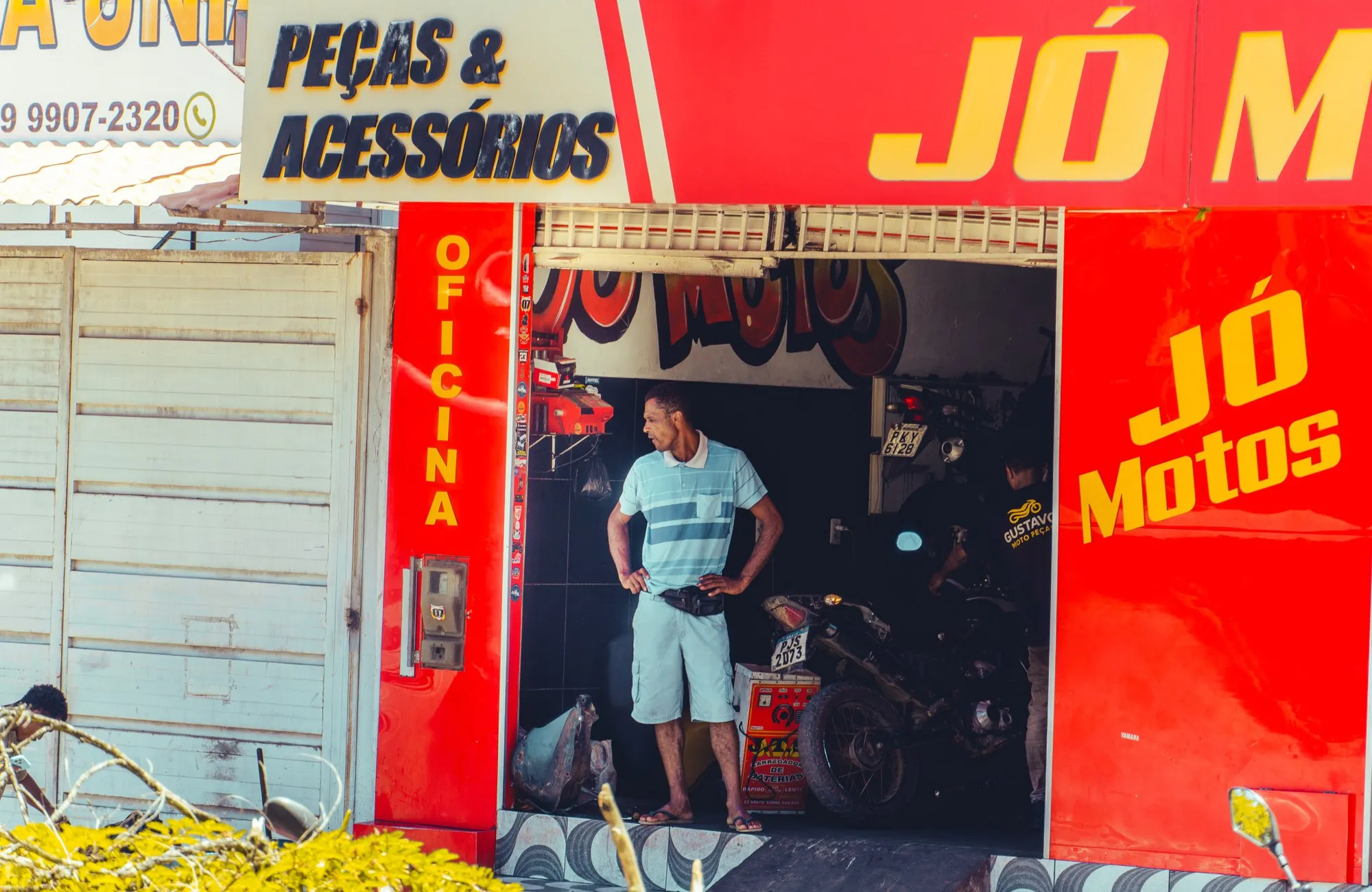 Un mécanicien se tient à l'entrée d'un garage de motos à la façade rouge et jaune.