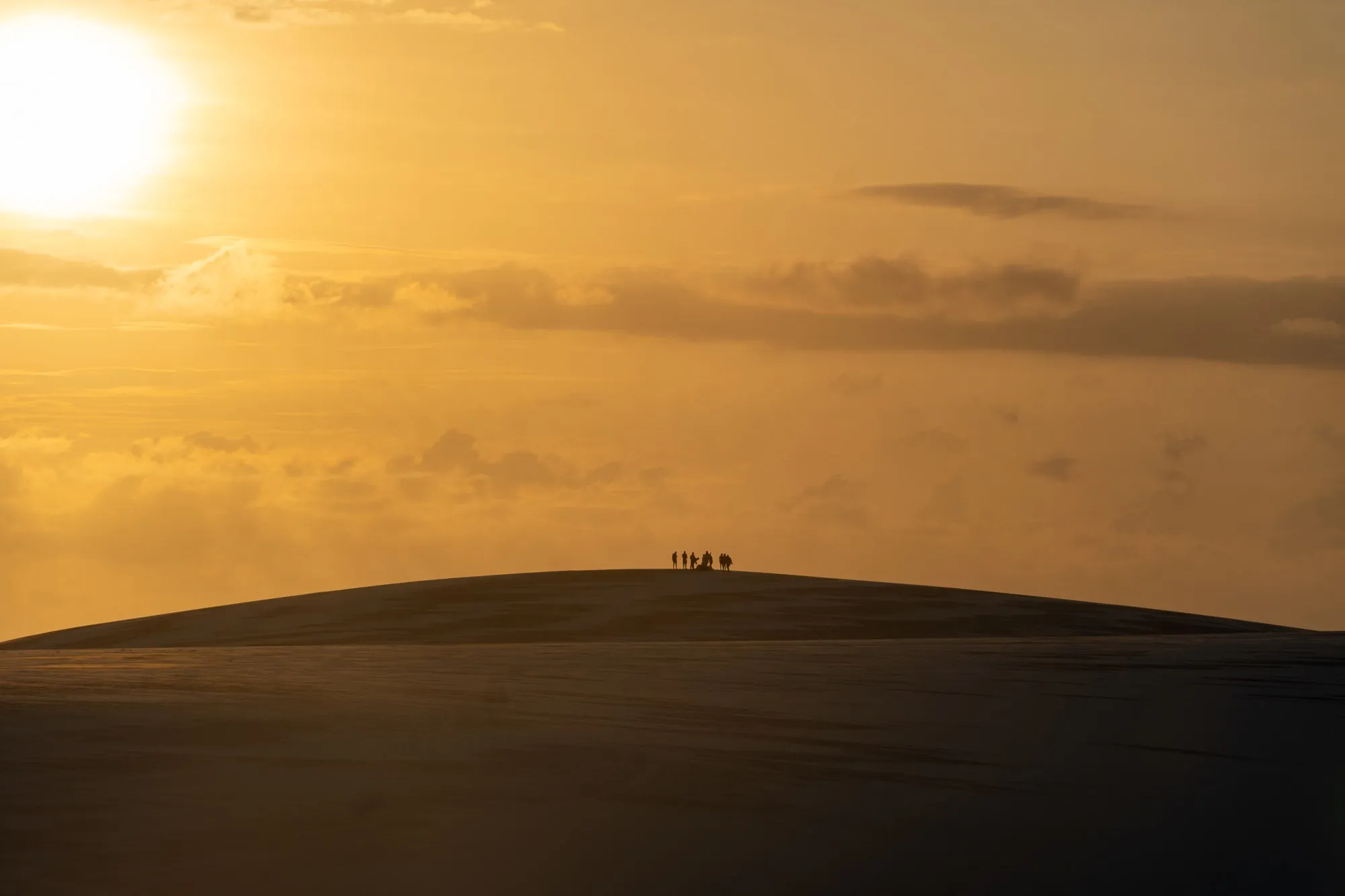 Des silhouettes minuscules au sommet d'une dune, sous un soleil orangé.