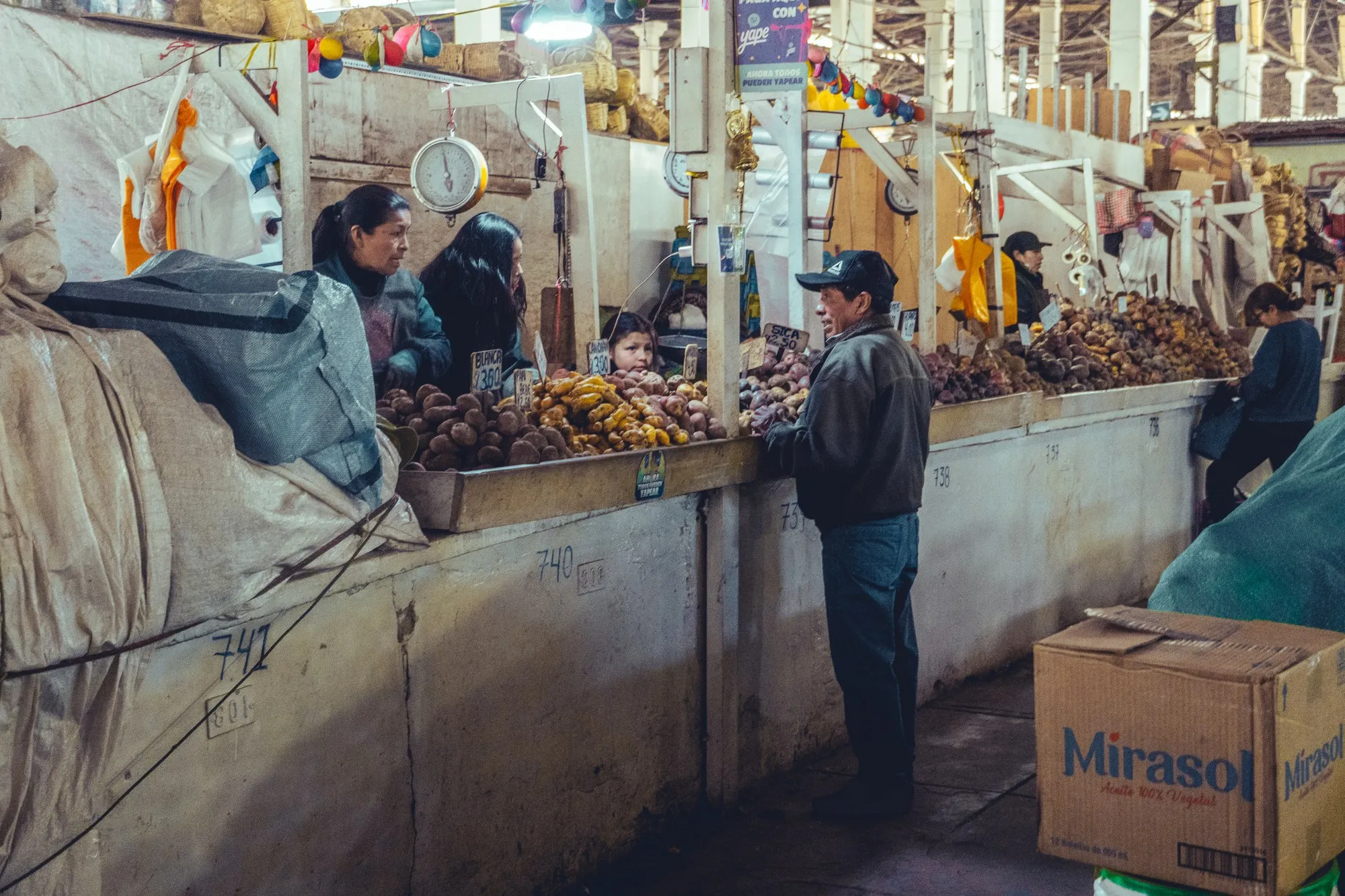 Une allée de marché couvert, un homme en casquette attend devant un étal.