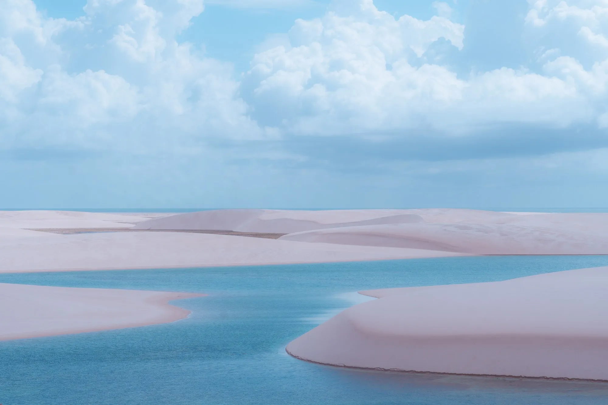 Des dunes blanches et roses bordent des lagunes turquoise sous un ciel nuageux.