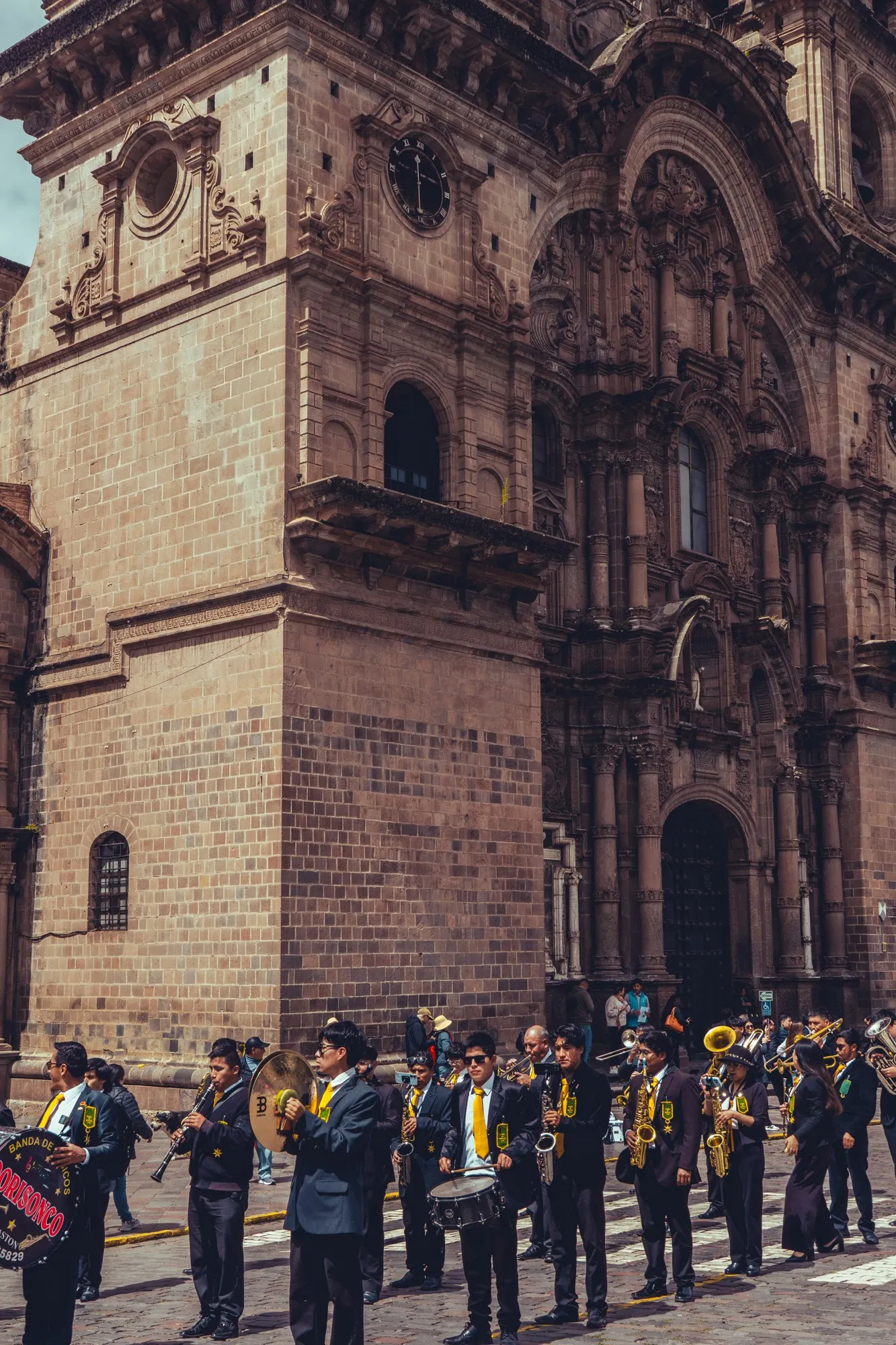 Une fanfare en uniforme joue devant la façade sculptée d'une église coloniale.