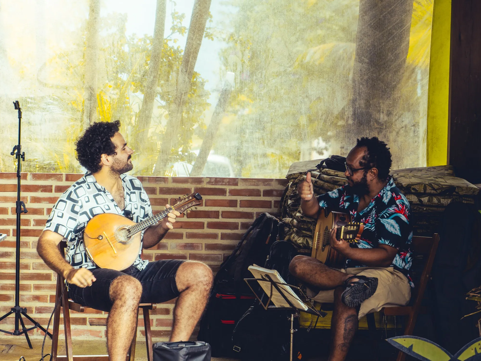 Deux musiciens jouent, l'un d'un bandolim, l'autre d'une guitare, devant un mur de briques.