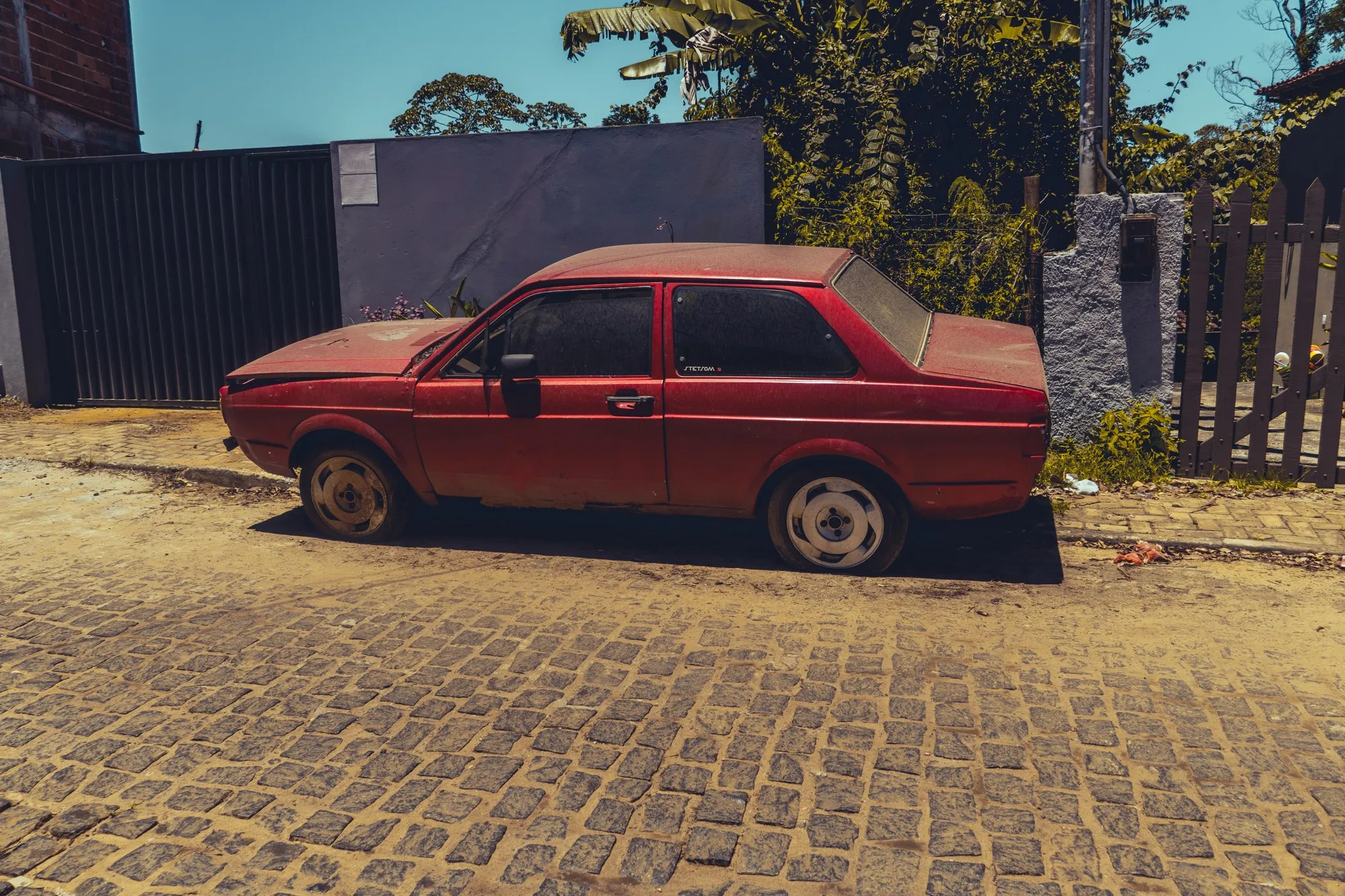 Une vieille voiture rouge couverte de poussière sur des pavés.