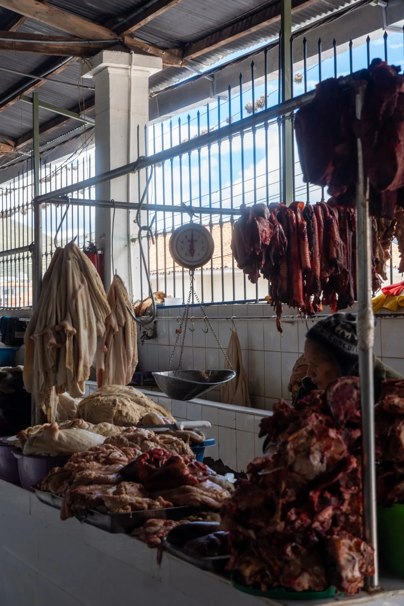Des pièces de viande suspendues à des crochets au-dessus d'un étal carrelé.