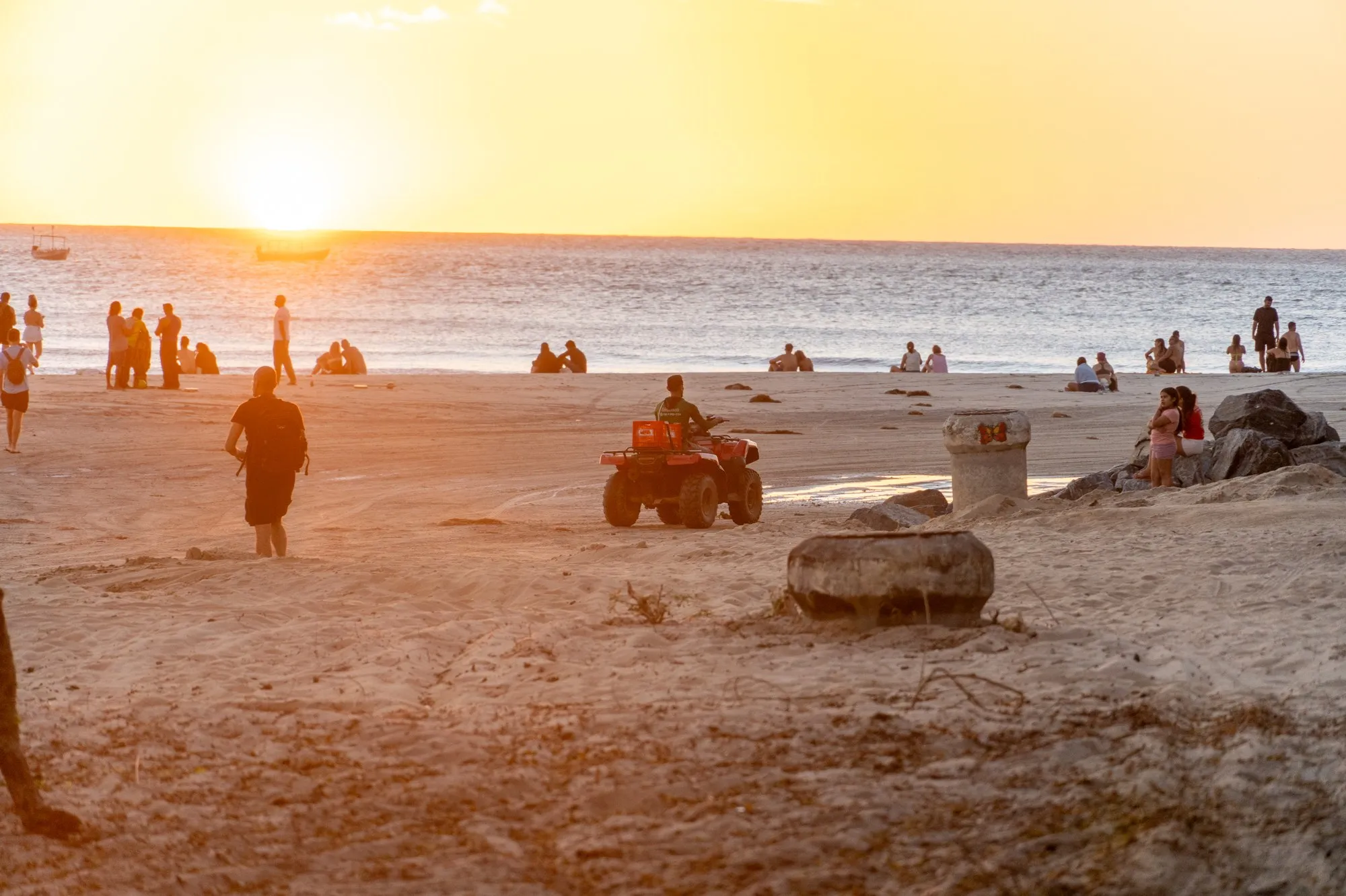 Une plage au coucher du soleil, un quad et des promeneurs sur le sable doré.