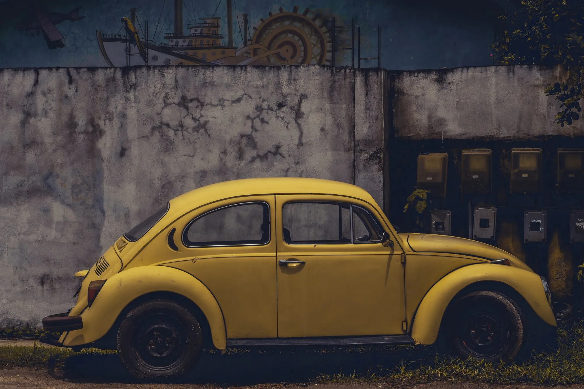 Une Coccinelle jaune garée devant un mur gris décoré d'un soleil peint.