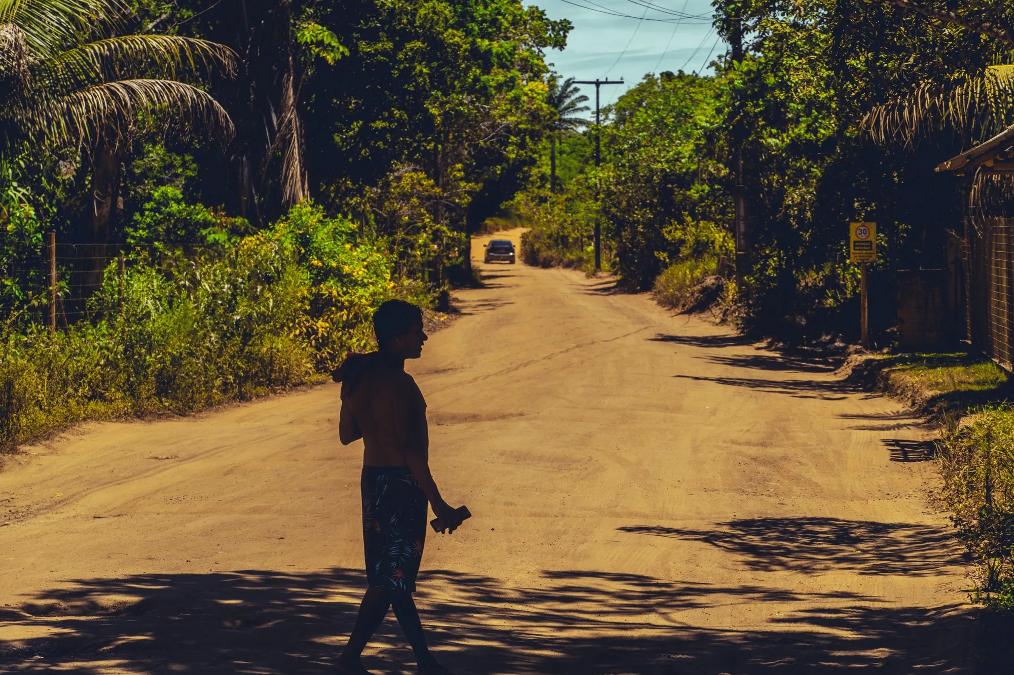 Un garçon marche sur une route de terre bordée de végétation.