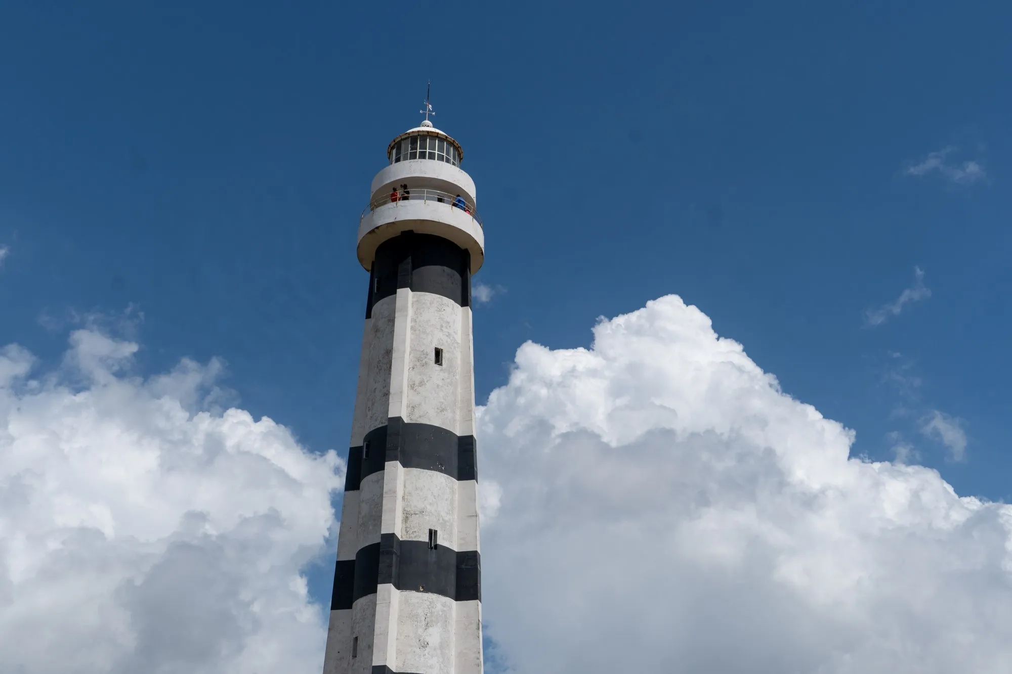 Un phare rayé noir et blanc se dresse devant de gros nuages blancs sur un ciel bleu profond.